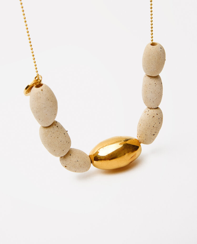 Colección TERRA.
- KALA es luz y tierra entrelazadas. Collar de cerámica en gres, con formas ovaladas que evocan suavidad y armonía. Cada pieza, vestida con lustre de oro, captura un instante donde lo orgánico se encuentra con lo precioso. KALA es elegancia hecha a mano, un reflejo de fuerza y delicadeza..
&nbsp;Collar realizado en gres y cocido a  1260ºC. Lustrados en oro.Compuesto por 6 piezas de gres natural (2x1cm) y pieza lustrada en oro de 2,5 x 1,3 cm). Montada en cadena de plata bañada en oro.&nbsp;&nbsp;
Piezas únicas de cerámica realizadas mediante un proceso artesanal
En La Polaca, cada creación nace de un cuidadoso proceso artesanal. Trabajamos la porcelana, gres y arcillas a mano, modelando, esmaltando, lustrando y dando forma a cada detalle con dedicación y sensibilidad. Cada pieza evoluciona de manera natural en el taller, siguiendo el ritmo del oficio cerámico.
El resultado es siempre una pieza única, con matices, texturas y pequeñas variaciones que le otorgan personalidad propia.