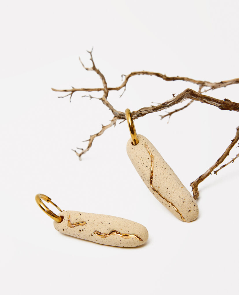Colección TERRA.
- VARA es tierra que recuerda. Pendientes de cerámica donde una raíz deja su huella, marcada en lustre de oro como un trazo sagrado.Una pieza que celebra la conexión entre origen y luz, entre lo que nace profundo y lo que brilla en la superficie. VARA es memoria dorada sobre arcilla viva. 
&nbsp;Pendientes realizado en gres y cocido a 1220ºC y 1260ºC. Lustrados en oro.Tamaño de las piezas entre 5 y 1,2 cm. Aros de acero inoxidable.&nbsp;
Piezas únicas de cerámica realizadas mediante un proceso artesanal
En La Polaca, cada creación nace de un cuidadoso proceso artesanal. Trabajamos la porcelana, gres y arcillas a mano, modelando, esmaltando, lustrando y dando forma a cada detalle con dedicación y sensibilidad. Cada pieza evoluciona de manera natural en el taller, siguiendo el ritmo del oficio cerámico.
El resultado es siempre una pieza única, con matices, texturas y pequeñas variaciones que le otorgan personalidad propia.