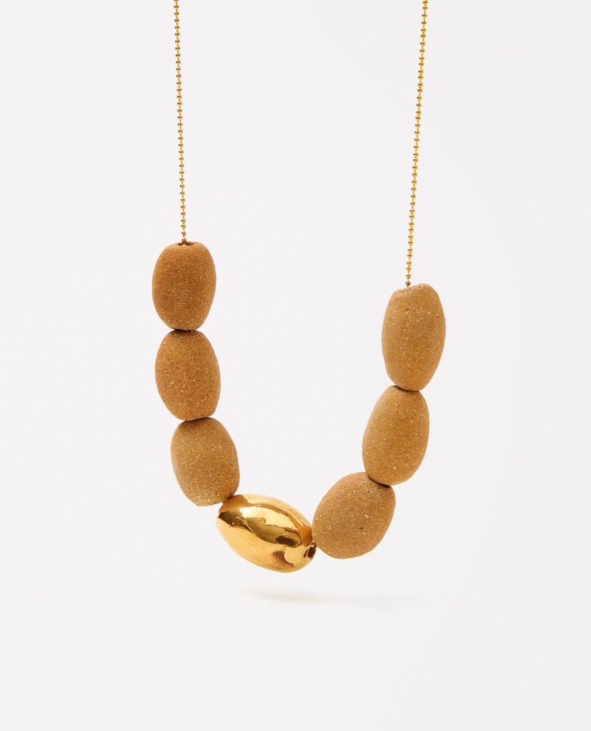 Colección TERRA.
- KALA es luz y tierra entrelazadas. Collar de cerámica en gres, con formas ovaladas que evocan suavidad y armonía. Cada pieza, vestida con lustre de oro, captura un instante donde lo orgánico se encuentra con lo precioso. KALA es elegancia hecha a mano, un reflejo de fuerza y delicadeza..
&nbsp;Collar realizado en gres y cocido a  1260ºC. Lustrados en oro.Compuesto por 6 piezas de gres natural (2x1cm) y pieza lustrada en oro de 2,5 x 1,3 cm). Montada en cadena de plata bañada en oro.&nbsp;&nbsp;
Piezas únicas de cerámica realizadas mediante un proceso artesanal
En La Polaca, cada creación nace de un cuidadoso proceso artesanal. Trabajamos la porcelana, gres y arcillas a mano, modelando, esmaltando, lustrando y dando forma a cada detalle con dedicación y sensibilidad. Cada pieza evoluciona de manera natural en el taller, siguiendo el ritmo del oficio cerámico.
El resultado es siempre una pieza única, con matices, texturas y pequeñas variaciones que le otorgan personalidad propia.