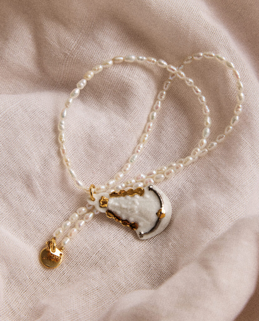 REGINA CAELI (Reina del cielo).
Collar medalla Virgen del Rocío, modelada y pintada a mano, realizada en PORCELANA, cocida a 1230 grados y lustrada en ORO y PLATA.Collar de perla natural forma orgánica 5mm..Medidas de la medalla: 3,5 x 2,5 cm.Medidas longitud collar: 46cm.&nbsp;
Piezas únicas de cerámica realizadas mediante un proceso artesanal
En La Polaca, cada creación nace de un cuidadoso proceso artesanal. Trabajamos la porcelana, gres y arcillas a mano, modelando, esmaltando, lustrando y dando forma a cada detalle con dedicación y sensibilidad. Cada pieza evoluciona de manera natural en el taller, siguiendo el ritmo del oficio cerámico.
El resultado es siempre una pieza única, con matices, texturas y pequeñas variaciones que le otorgan personalidad propia.