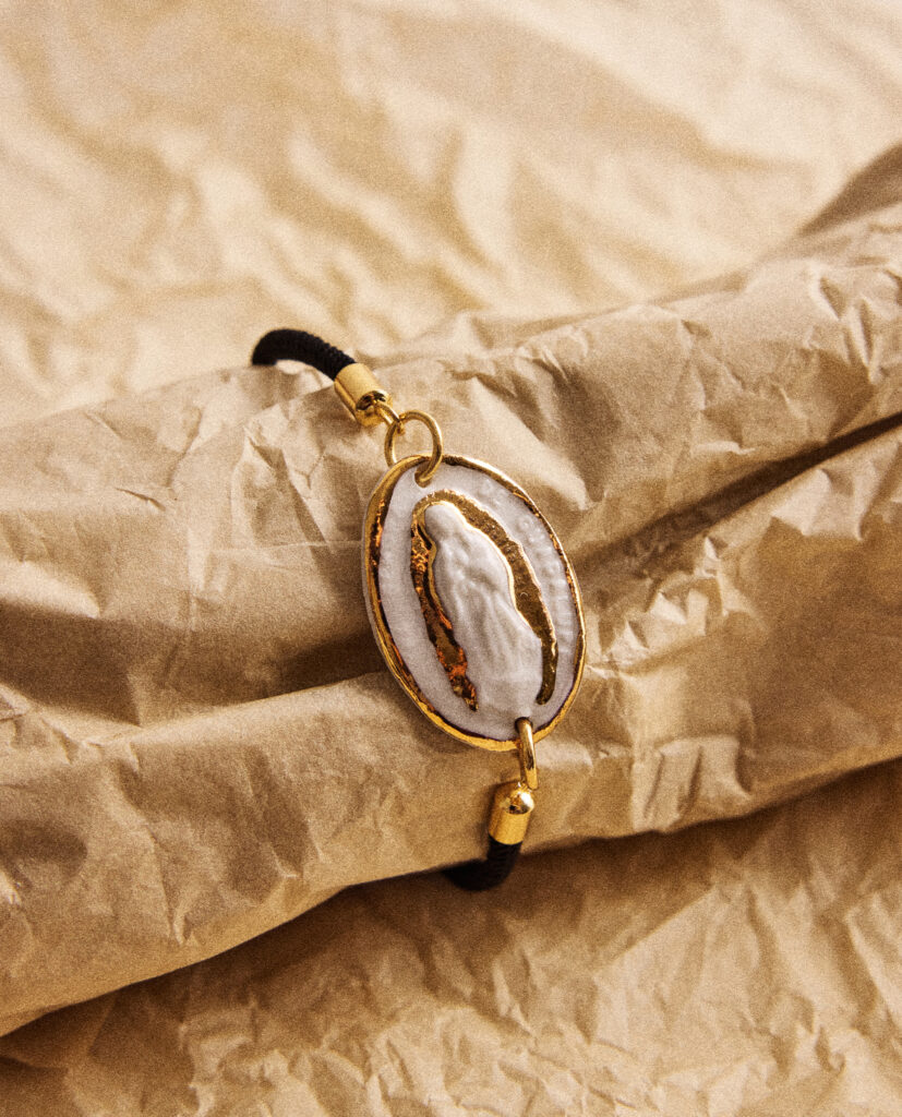 REGINA CAELI (Reina del cielo).
Pulsera medalla  Virgen de Guadalupe, modelada y pintada a mano, realizada en porcelana, cocida a 1230 grados y lustrada en oro.Cordón ajustable con acabados de acero dorado.(El tono del cordón puedes elegirlo dejando el color en comentarios: negro, marrón,  azul o granate).Medidas de la medalla: 3 x 2 cm.&nbsp;
Piezas únicas de cerámica realizadas mediante un proceso artesanal
En La Polaca, cada creación nace de un cuidadoso proceso artesanal. Trabajamos la porcelana, gres y arcillas a mano, modelando, esmaltando, lustrando y dando forma a cada detalle con dedicación y sensibilidad. Cada pieza evoluciona de manera natural en el taller, siguiendo el ritmo del oficio cerámico.
El resultado es siempre una pieza única, con matices, texturas y pequeñas variaciones que le otorgan personalidad propia.