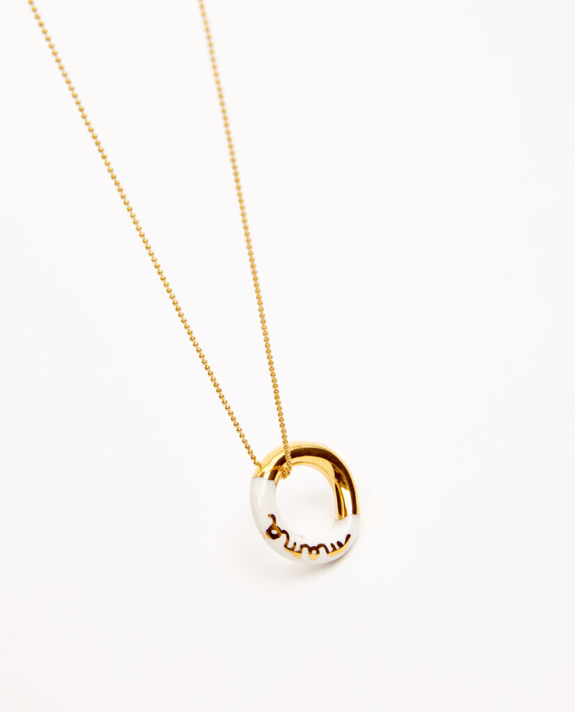 Pieza cerámica esmaltada en brillo lustrada en oro. Palabra mamá. Cadena de plata bañada en oro 16k.Diámetro aproximado del aro 15mm.  Largo de la cadena: 210mm.&nbsp;
Piezas únicas de cerámica realizadas mediante un proceso artesanal
En La Polaca, cada creación nace de un cuidadoso proceso artesanal. Trabajamos la porcelana, gres y arcillas a mano, modelando, esmaltando, lustrando y dando forma a cada detalle con dedicación y sensibilidad. Cada pieza evoluciona de manera natural en el taller, siguiendo el ritmo del oficio cerámico.