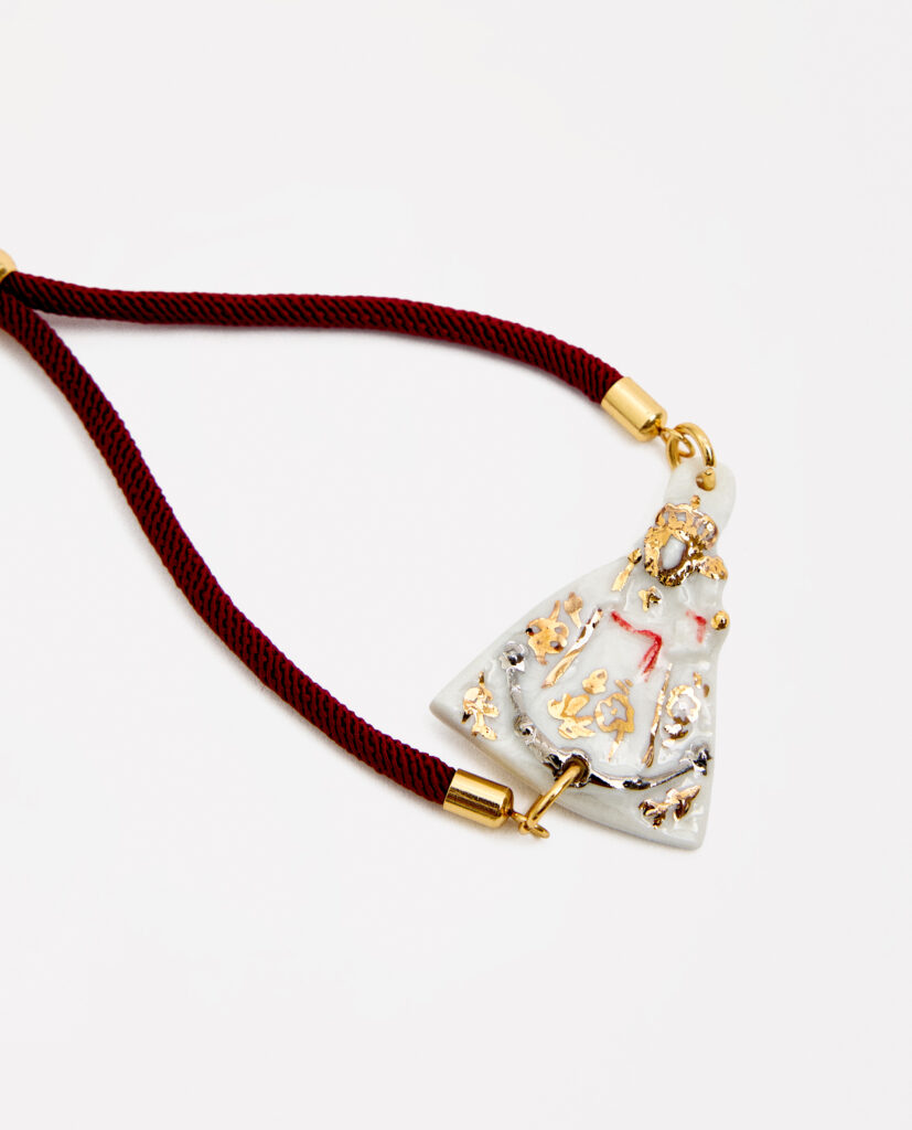REGINA CAELI (Reina del cielo).
Pulsera  Virgen de la Fuensanta, modelada y pintada a mano, realizada en porcelana, cocida a 1230 grados y lustrada en oro y plata.Cordón ajustable con acabados de acero dorado.Disponible en dos tonos de cordón: marrón o negro.Medidas de la medalla: 3,7 x 2,7 cm.&nbsp;
Piezas únicas de cerámica realizadas mediante un proceso artesanal
En La Polaca, cada creación nace de un cuidadoso proceso artesanal. Trabajamos la porcelana, gres y arcillas a mano, modelando, esmaltando, lustrando y dando forma a cada detalle con dedicación y sensibilidad. Cada pieza evoluciona de manera natural en el taller, siguiendo el ritmo del oficio cerámico.
El resultado es siempre una pieza única, con matices, texturas y pequeñas variaciones que le otorgan personalidad propia.